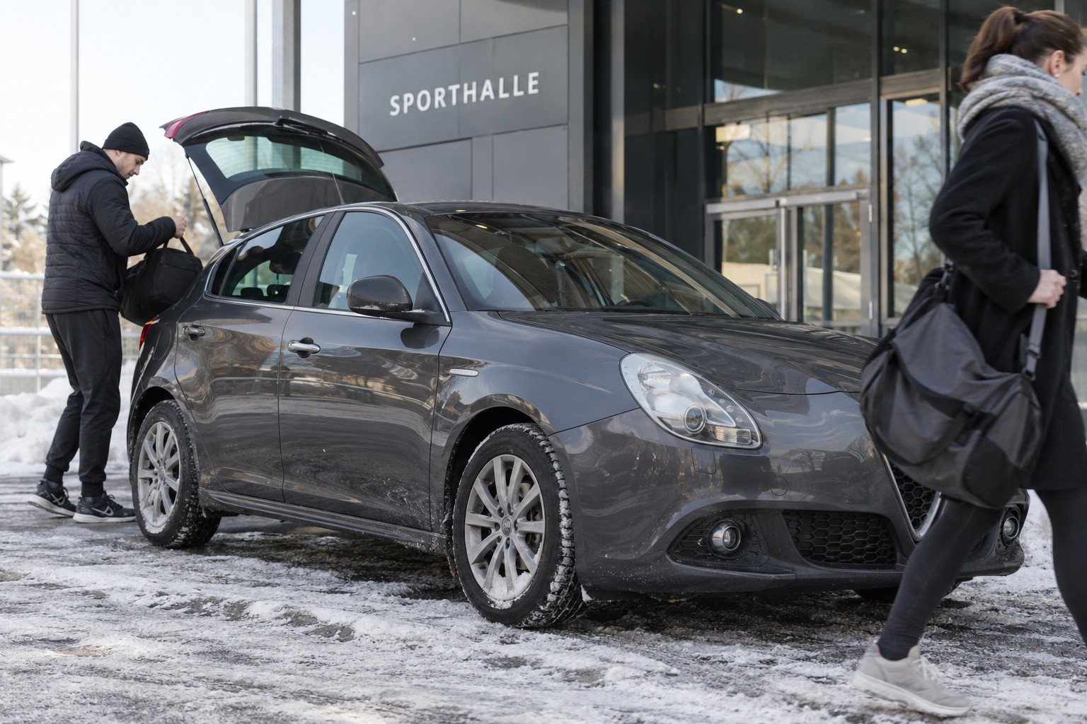 Alfa Romeo Giulietta: Giulietta-Motoren und Sportausführungen verlangen eigene Fahrzeugdaten; Änderungen an Leistung oder Fahrwerk angeben. Dunkelgrauer Alfa Romeo Giulietta vor einer Sporthalle mit Sporttasche