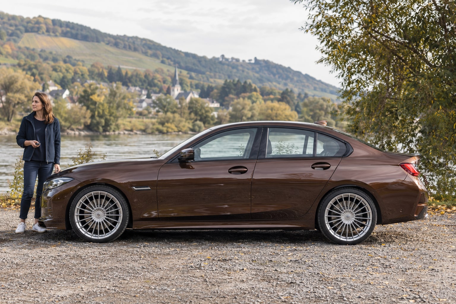 Alpina Autoversicherung: Herstellerkennung, Sonderausstattung und dokumentierten Fahrzeugwert gemeinsam prüfen. Alpina Autoversicherung: Braune Limousine mit Frau am Flussufer