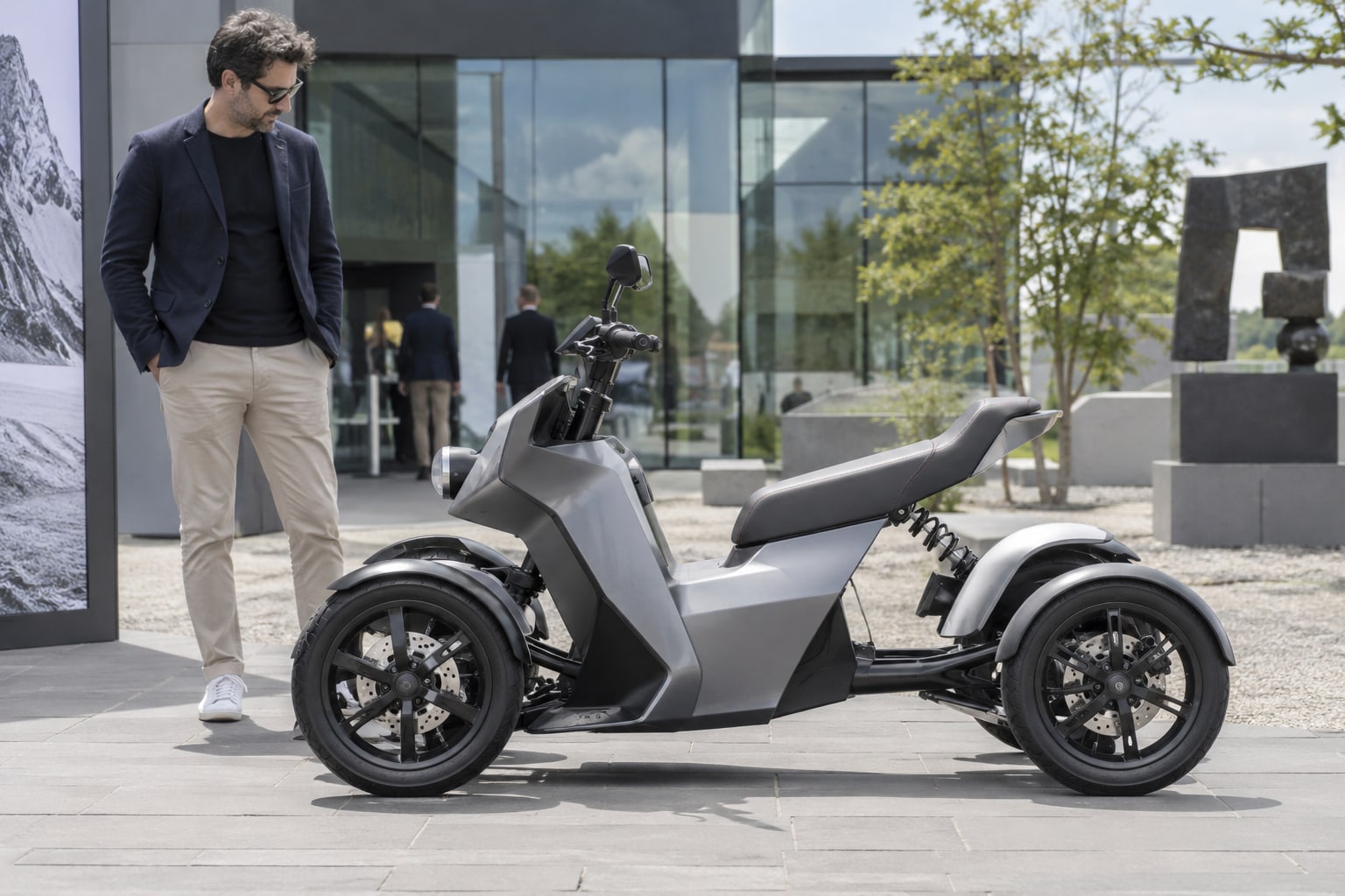 Artega Karo Versicherung: Konzeptidentität und genehmigte Fahrzeugklasse statt einer pauschalen Pkw-Zuordnung prüfen. Artega Karo: offenes silbernes elektrisches Quad-Konzept mit Mann vor einem Glasgebäude