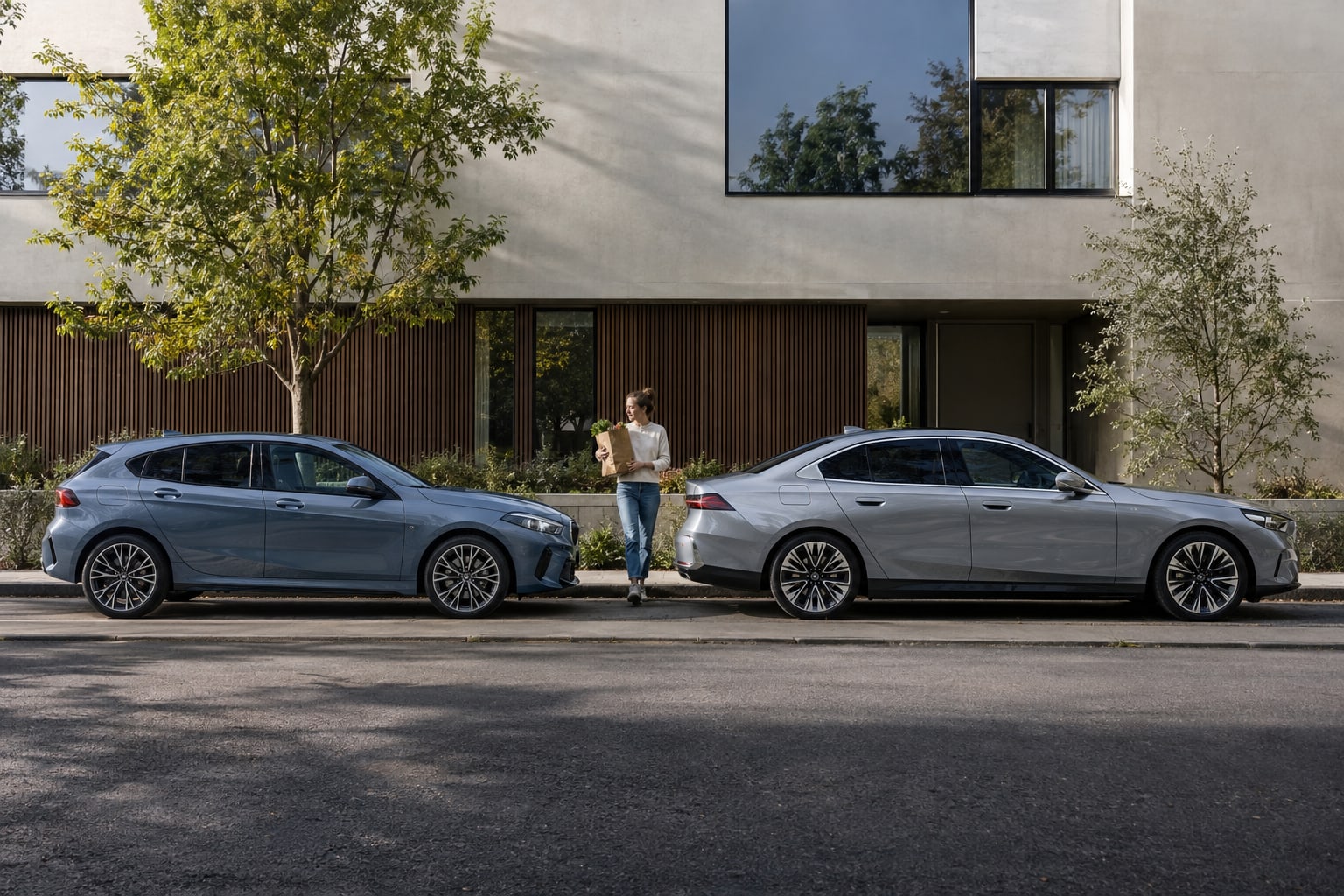 BMW Autoversicherung: Welche Unterschiede zeigen Typklassen von 1er, 3er, 5er, X1 und X3? Blauer Kompaktwagen und silberne Limousine in Seitenansicht an einer modernen Hausfassade