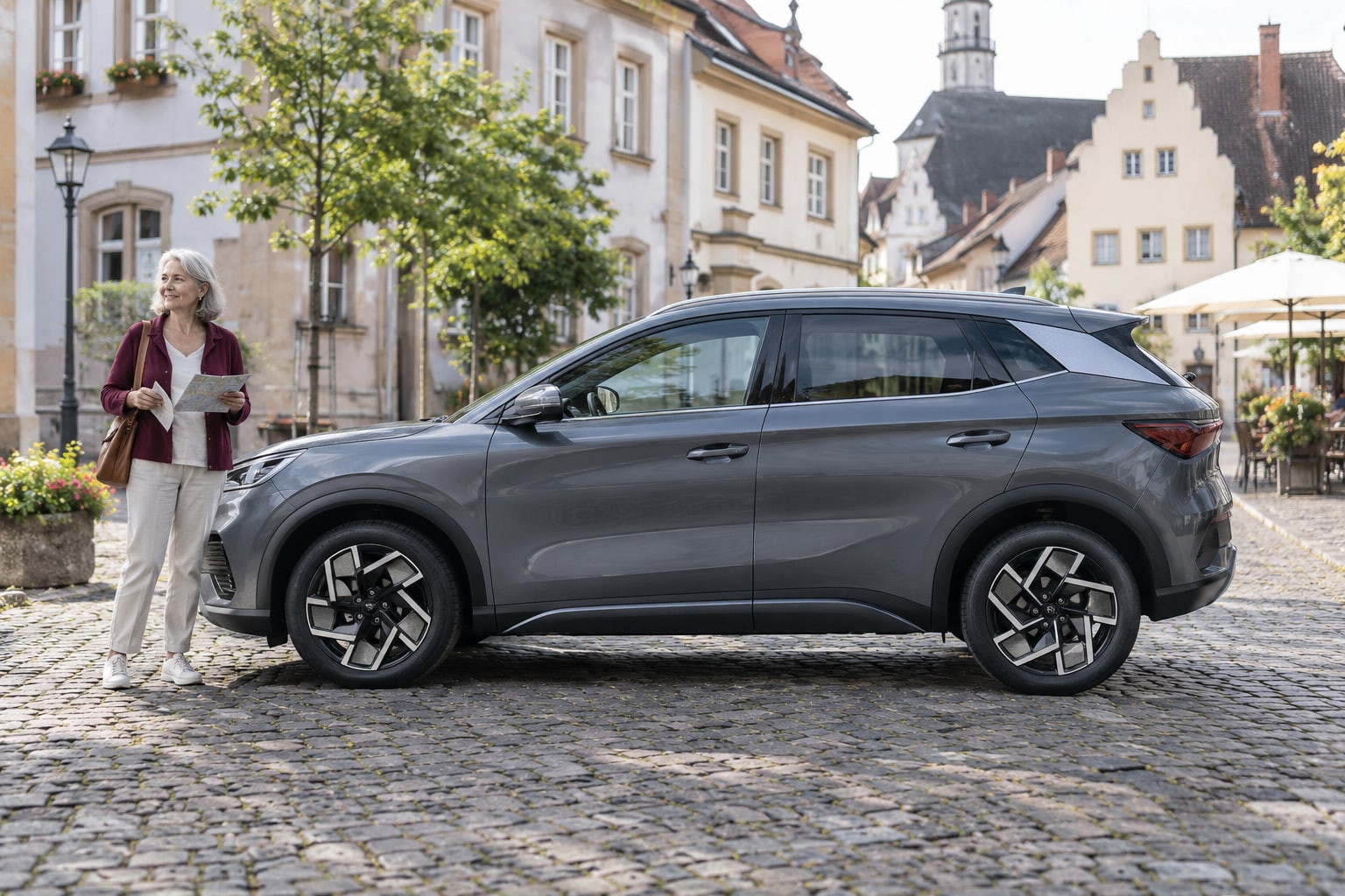 BYD ATTO 3 Autoversicherung: Die vorhandene Generation vor der Auswahl von Antrieb und Kaskoschutz feststellen. Grauer kompakter Elektro-SUV mit Frau auf einem Stadtplatz: BYD Atto 3 Kfz-Versicherung