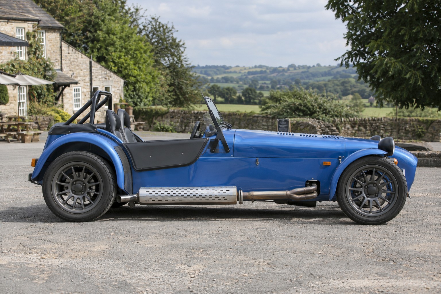 Caterham Seven: zugelassenen Aufbau, Fahrzeugwert und Straßennutzung dokumentieren. Blauer Caterham Seven im Seitenprofil vor einem Landgasthof