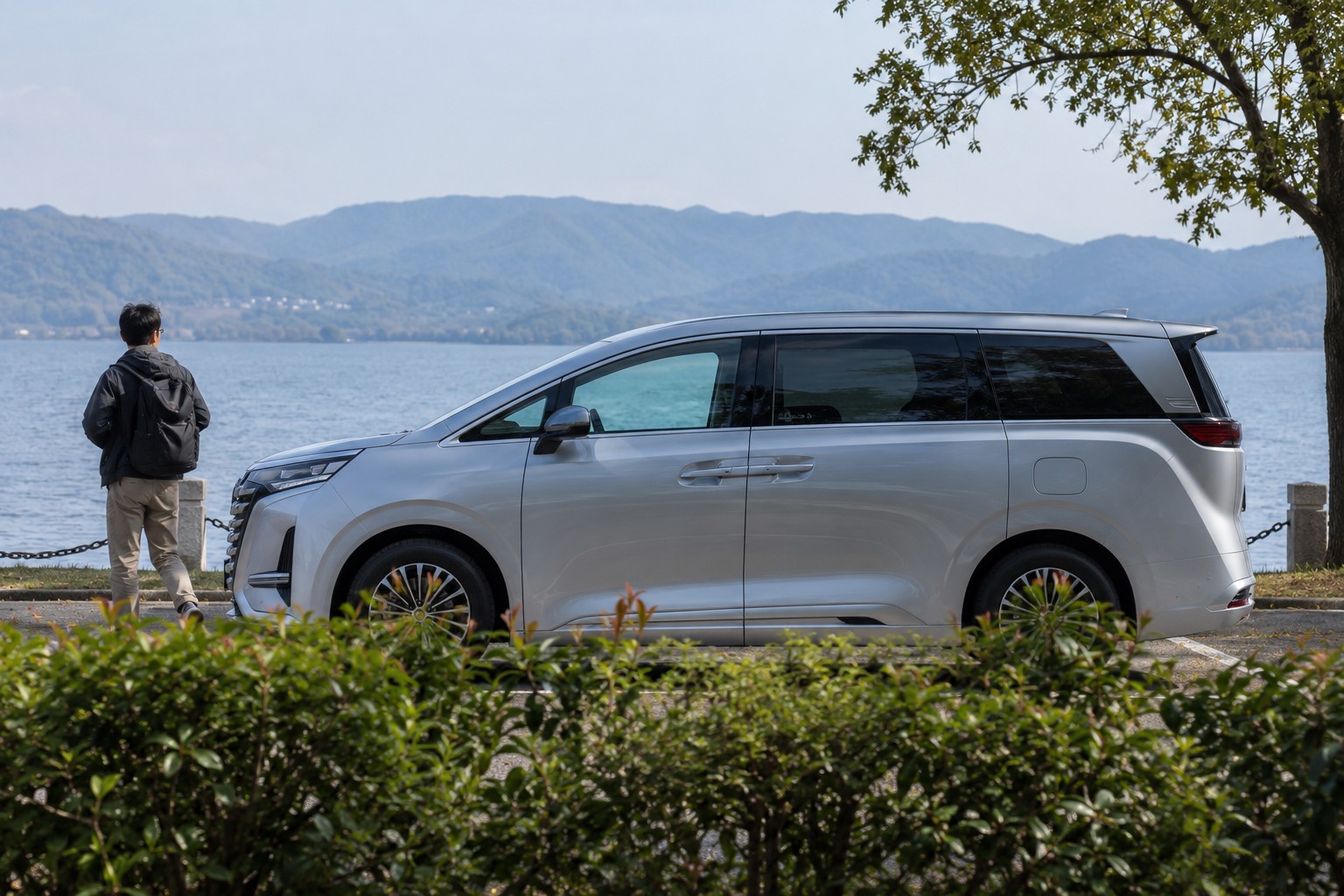 Denza D9 Autoversicherung: D9 als Familienauto oder Chauffeurfahrzeug versichern Mann neben einem silbernen Denza D9 an einer Seepromenade