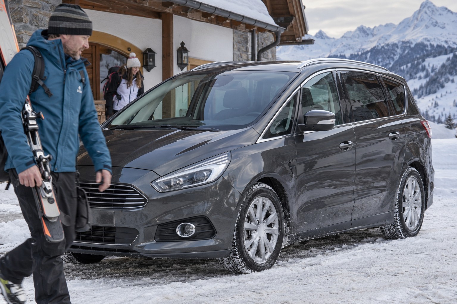 Dunkelgrauer Ford S-MAX vor einem verschneiten Gasthaus mit Skiern