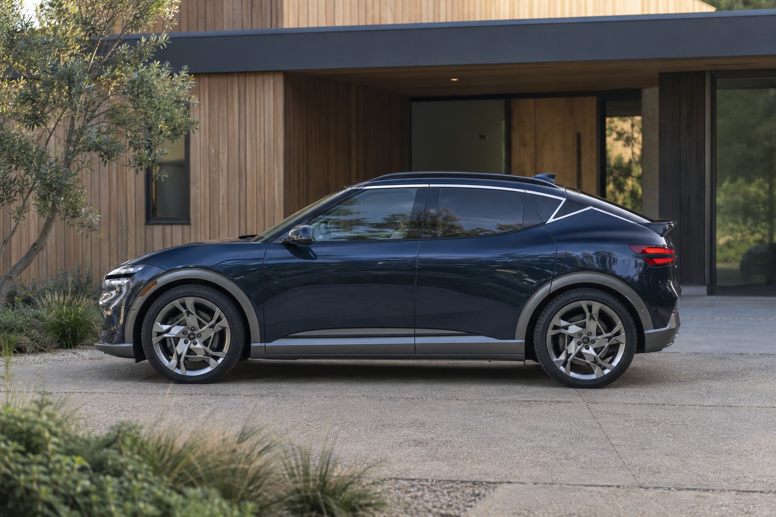 Dunkelblauer Genesis GV60 im Seitenprofil vor einem Holzhaus