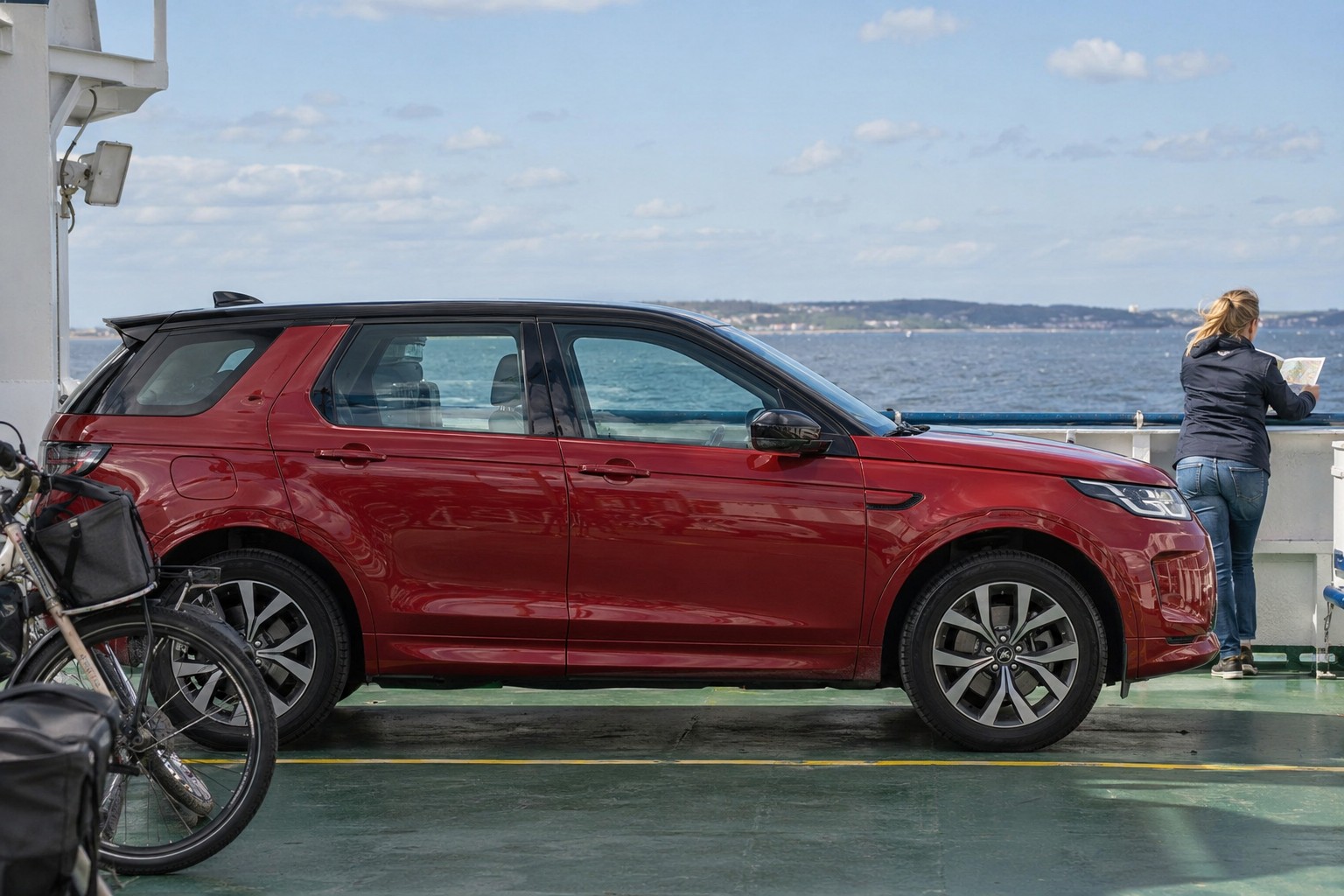 Land Rover Discovery Sport: Discovery Sport mit Plug-in-Hybridtechnik hat andere Antriebsdaten als die Dieselversionen der Modellfamilie. Roter Land Rover Discovery Sport auf einem Fährdeck neben einer Person mit Straßenkarte