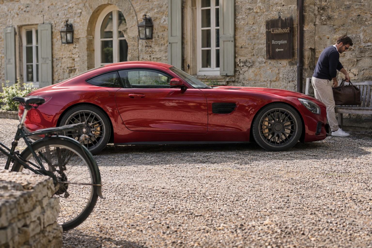 Mercedes-AMG GT Versicherung: Baureihen und Sonderausstattung Roter Mercedes-AMG GT der Baureihe C190 auf einem Kieshof neben einem Mann mit Reisetasche
