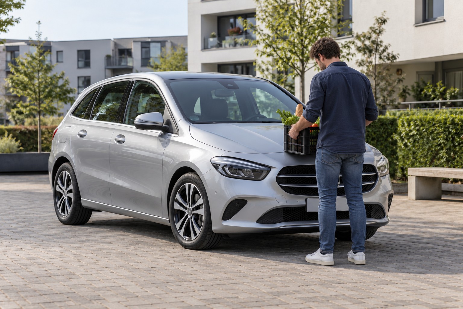 Mercedes B-Klasse Versicherung und Familienfahrer Silberne Mercedes-Benz B-Klasse in einem Wohnviertel; ein Mann hält eine Einkaufskiste