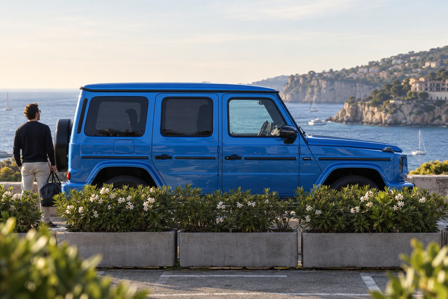 Mercedes-Benz G 580 mit EQ Technologie – Fahrzeug und Versicherung Mercedes-Benz G 580 mit EQ Technologie im Seitenprofil; blauer Wagen mit natürlichen Vordergrundpflanzen