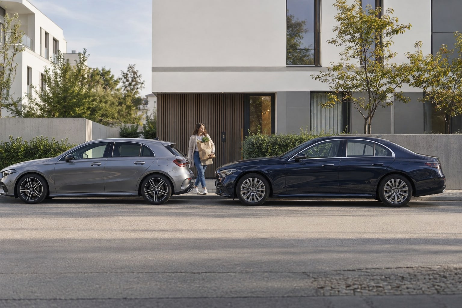 Mercedes-Benz Autoversicherung: Welche Leistungen zählen bei Leasing, Alltag und langen Strecken? Mercedes-Benz Autoversicherung: Grauer Kompaktwagen und dunkelblaue Limousine seitlich vor einer begrünten modernen Fassade