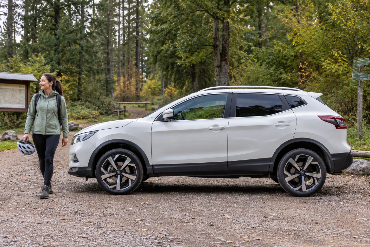 Nissan Autoversicherung: Silberner kompakter Crossover mit Frau vor einer Waldkulisse
