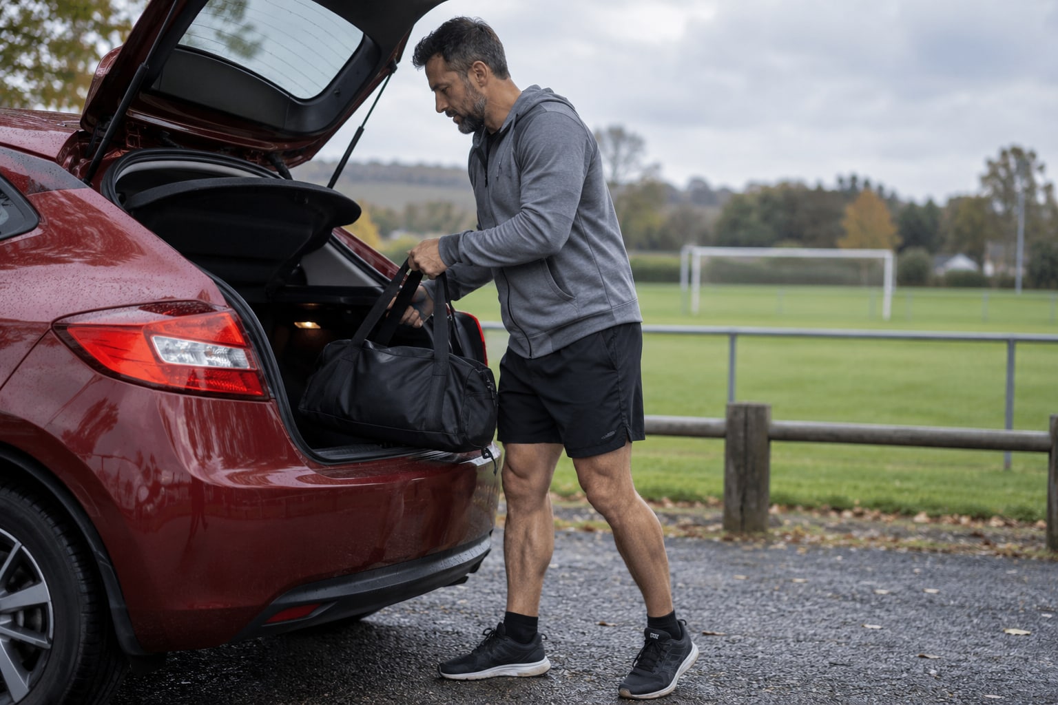 Sportler verstaut eine Tasche im roten Auto neben einem Fußballplatz