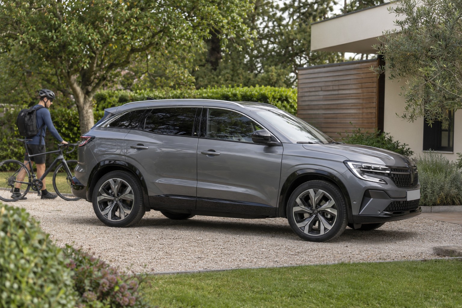 Renault Austral – E-Tech-Vollhybrid und Mildhybrid Grauer Renault Austral auf einer Hauseinfahrt, dahinter steht ein Radfahrer