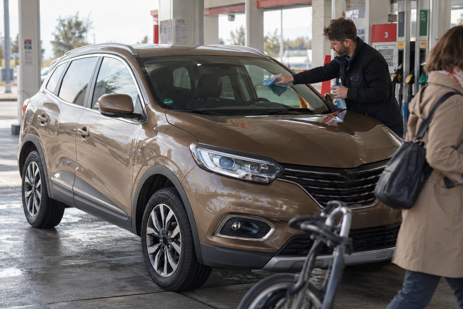 Bronzefarbener Renault Kadjar unter einem Tankstellendach beim Reinigen der Windschutzscheibe