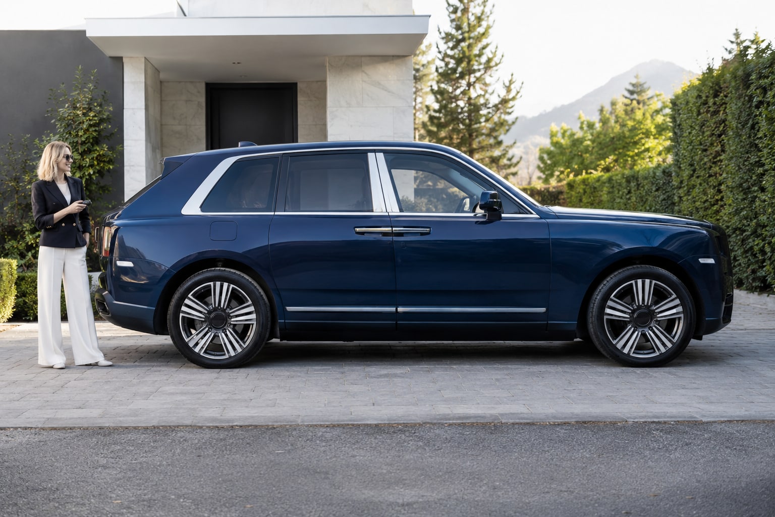 Rolls-Royce Cullinan Kfz-Versicherung: individuelle Heckausstattung und SUV-Nutzung abgleichen. Blauer großer SUV mit Frau vor einem Wohnhaus: Rolls-Royce Cullinan Kfz-Versicherung