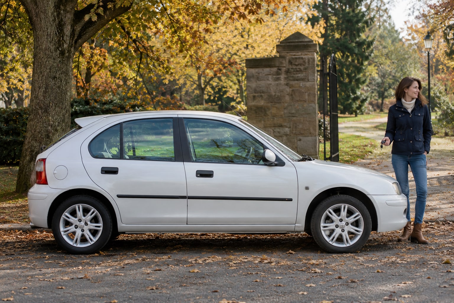 Rover Autoversicherung: Weißer Kompaktwagen mit Frau vor herbstlichen Bäumen