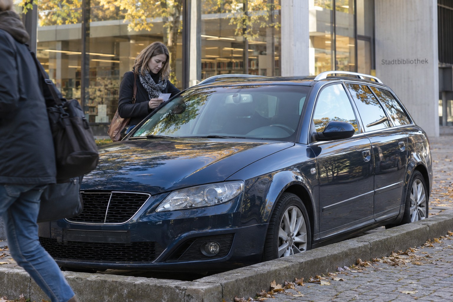 Dunkelblauer SEAT Exeo ST vor einer Bibliothek neben einer Frau mit Parkschein