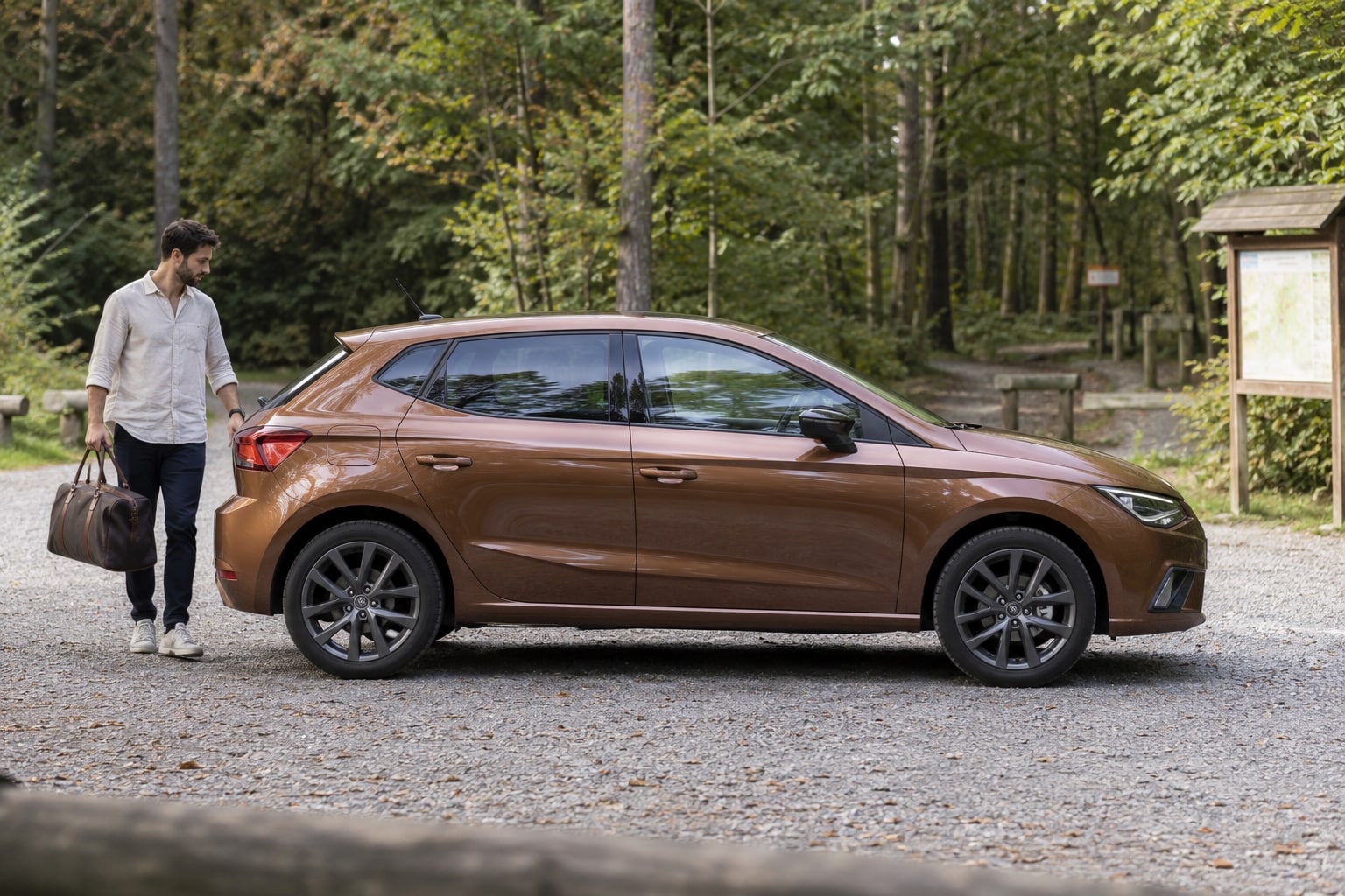SEAT Kfz-Versicherung: Ausstattungslinie und Antrieb gemeinsam betrachten. Bronzefarbener Schrägheckwagen mit Mann vor einer Waldkulisse: Seat Autoversicherung