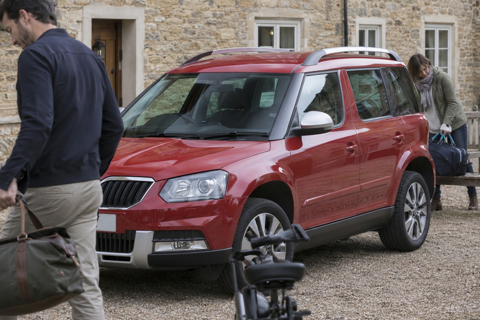 Škoda Yeti Versicherung: Frontantrieb und 4x4 Roter Škoda Yeti auf einem Kieshof mit Reisetasche und Holzbank