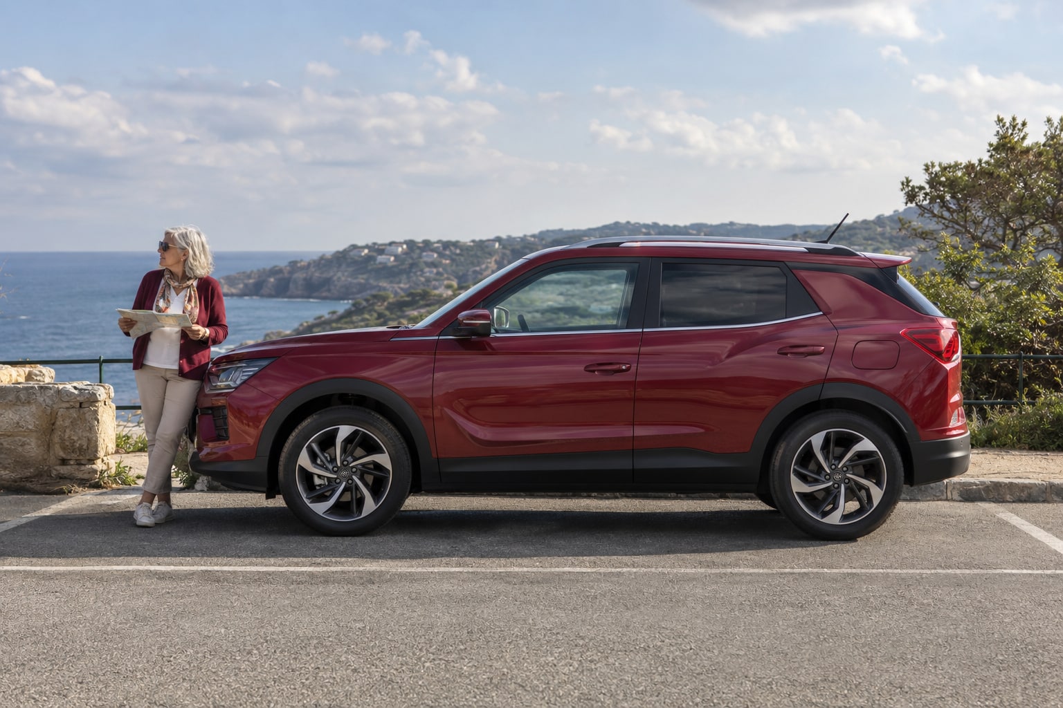 Korando Kfz-Versicherung: zugelassenen Verbrenner oder e-Motion mit eigener Generation erfassen. Bordeauxroter SUV mit Frau am See: SsangYong / KGM Korando Autoversicherung