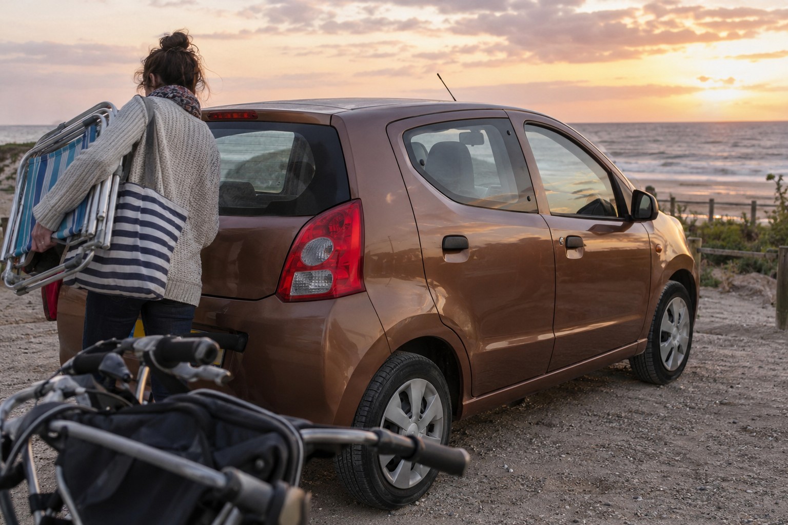 Suzuki Alto: Deutsche Alto-Ausführungen und Importe können andere Motor- und Zulassungsdaten haben. Bronzefarbener Suzuki Alto auf einem Parkplatz an der Küste mit Strandstühlen