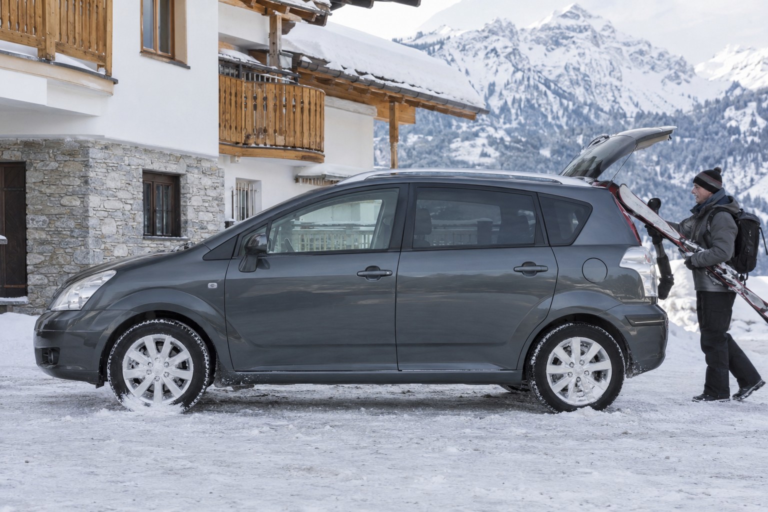 Toyota Corolla Verso: Corolla Verso, Verso und Verso-S dürfen nicht allein wegen ähnlicher Modellnamen gleichgesetzt werden. Dunkelgrauer Toyota Corolla Verso mit geöffnetem Kofferraum vor einem verschneiten Gasthaus