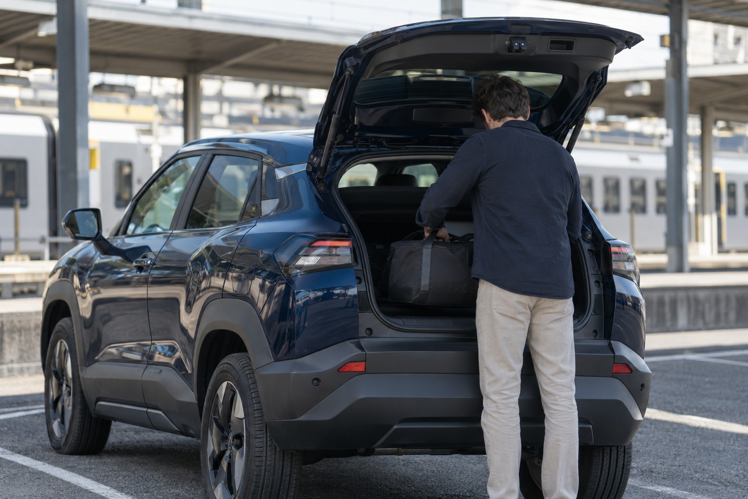 Mann mit Reisetasche am offenen Kofferraum eines blauen Toyota Urban Cruiser vor einem Bahnhof