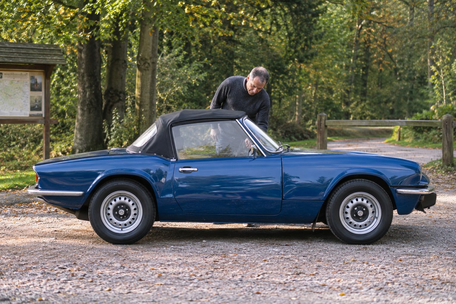 Blauer offener klassischer Roadster mit Mann vor einer Waldkulisse: Triumph Autoversicherung