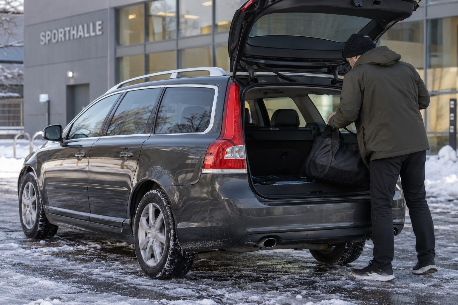 Dunkelgrauer Volvo V70 vor einer Sporthalle mit Sporttasche