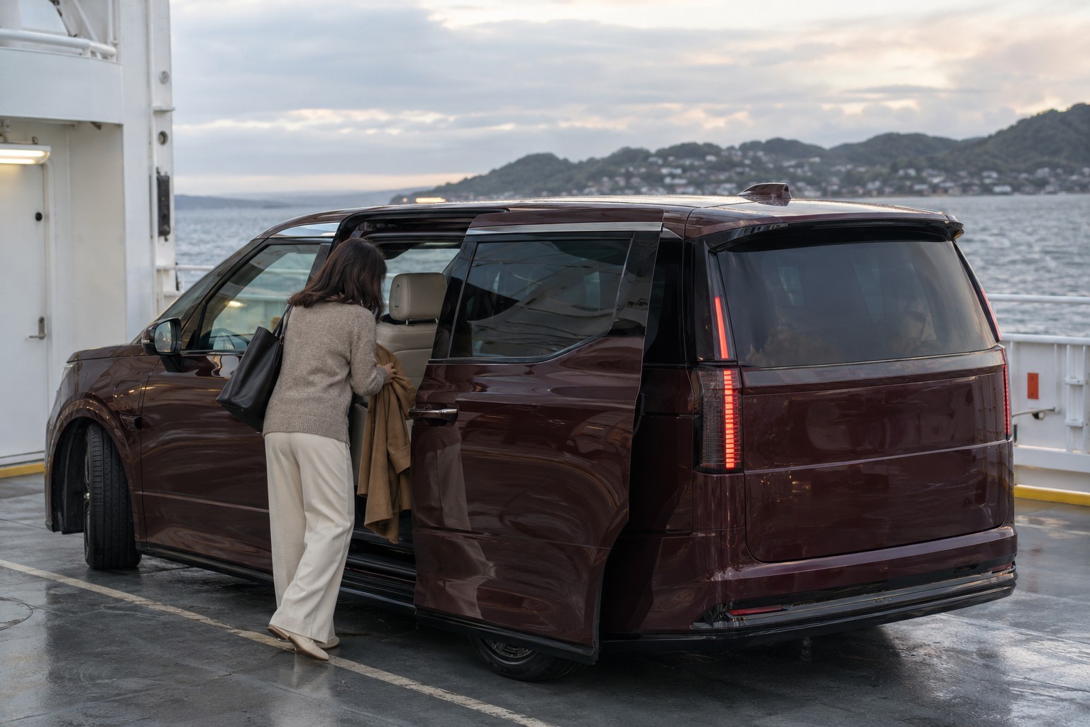 Frau an der geöffneten Schiebetür eines roten Volvo EM90 an einem Fährterminal