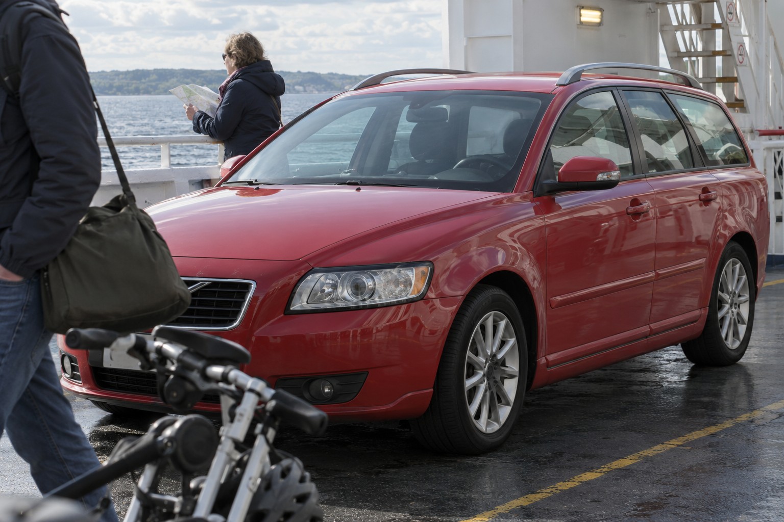 Roter Volvo V50 auf einem Fährdeck neben Reisenden und Fahrrädern