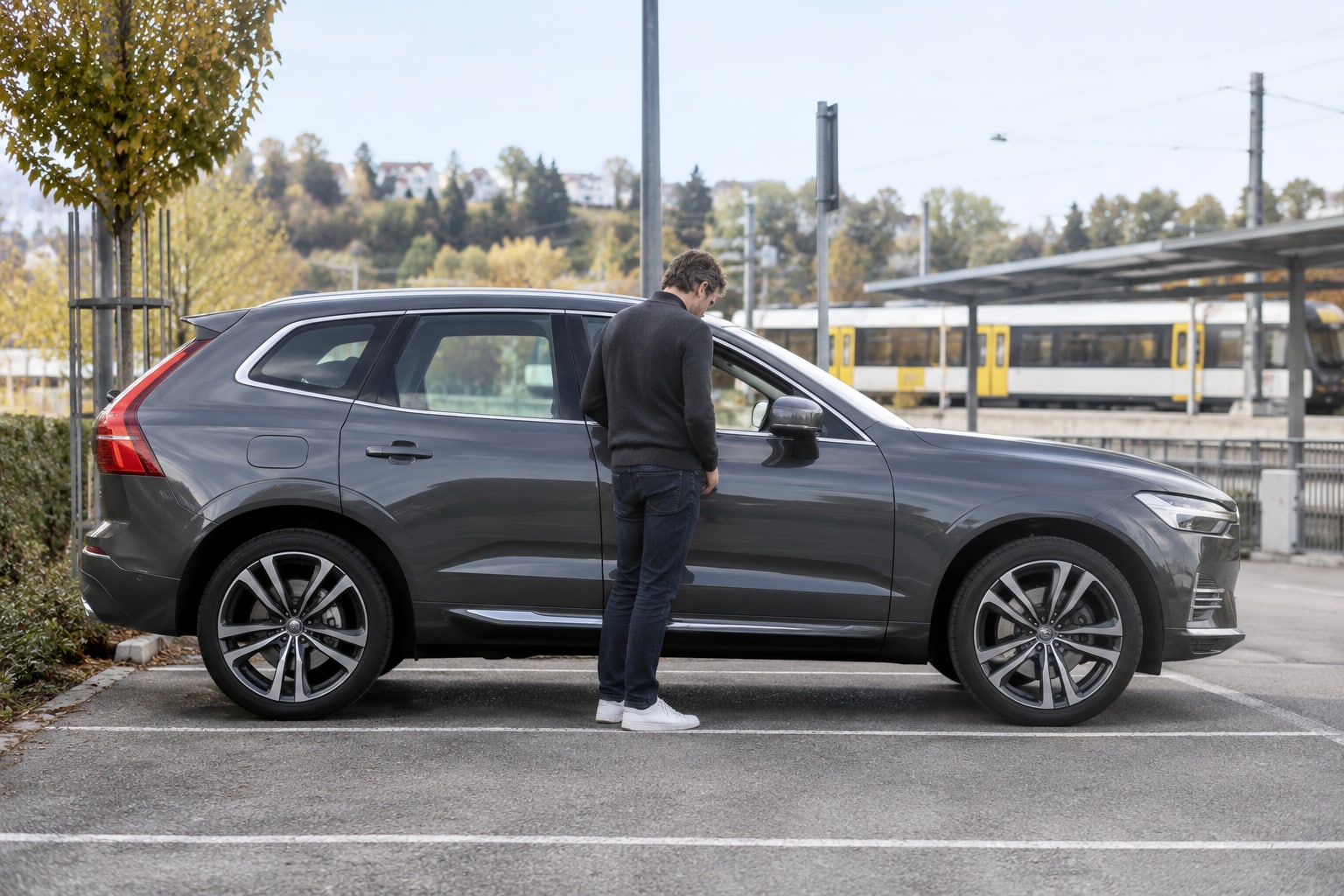 Volvo XC60 Kfz-Versicherung: Mildhybrid und Plug-in-SUV nach Ausstattung vergleichen. Grauer SUV mit Mann an einem überdachten Parkplatz: Volvo XC60 Autoversicherung