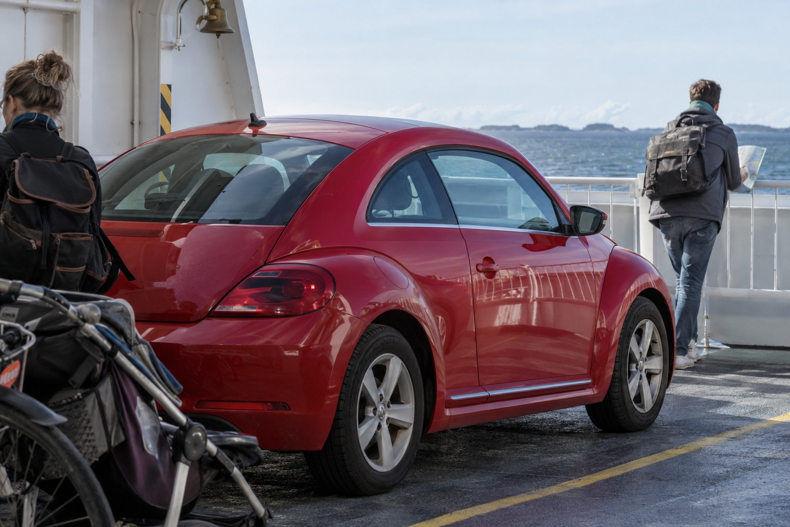VW Beetle Versicherung: Cabriolet und Sonderausstattung Roter VW Beetle auf einem Fährdeck neben einer Person mit Straßenkarte
