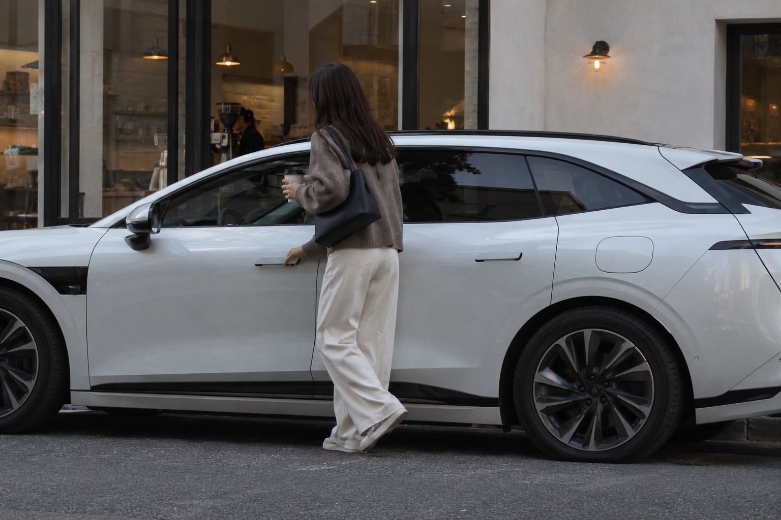 7GT Privilege AWD: Luftfederung und Reisebedarf bei Werkstattwahl und Kaskoleistungen berücksichtigen. Frau mit Kaffeebecher neben einem weißen Zeekr 7GT vor einem Café